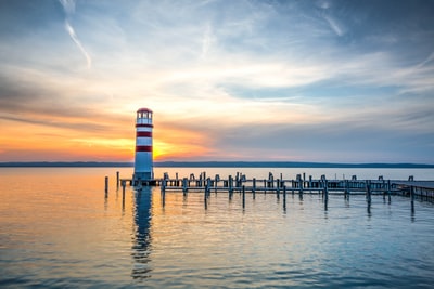 在清澈的蓝天下，木制海滩码头旁的白色和红色灯塔的照片
